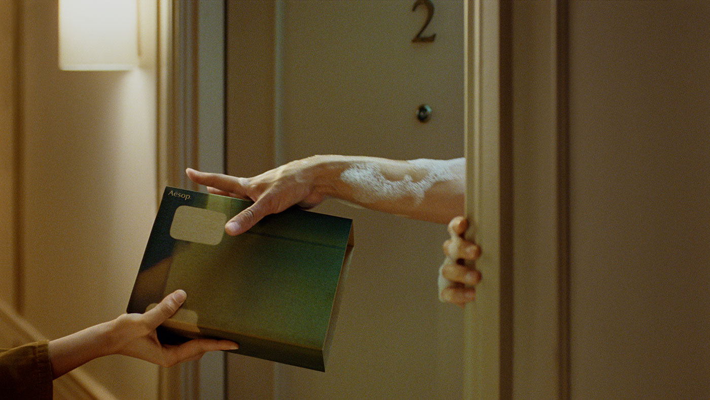 Two sets of hands exchange an Aesop Gift Kit at an apartment door
