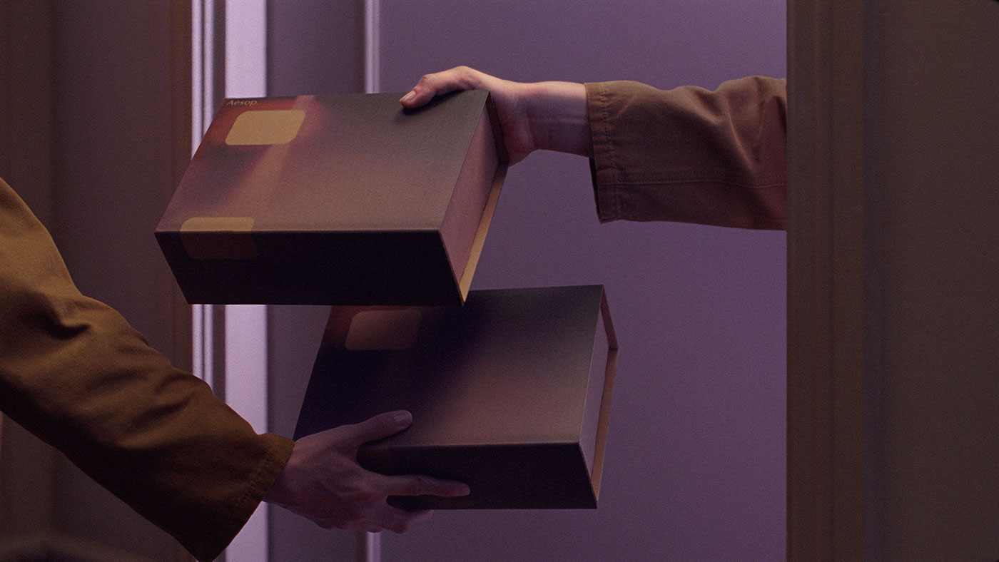 A sets of hands exchange two Aesop Gift Kits at an apartment door