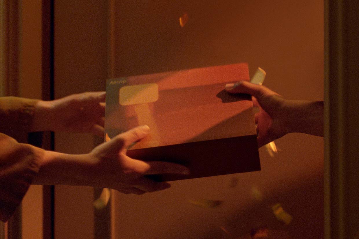 Two sets of hands exchange an Aesop Gift Kit at an apartment door
