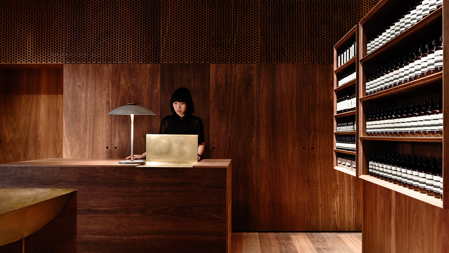 An Aesop consultant standing at a wooden counter and looking at a laptop 